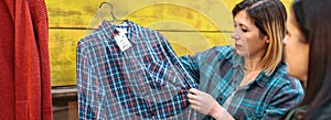 Banner of blonde woman employee showing plaid shirt to customer in vintage store