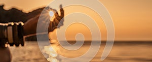 Banner. In blur closeup the hand of a young woman in bracelets. Practicing yoga on the beach with sunset. Keeps fingers