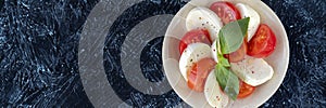 banner of caprese salad on a round plate. slices of juicy red tomato, with fresh mozzarella and basil leaves, poured