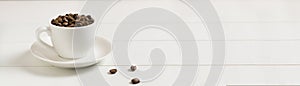 Banner Coffee beans in a white espresso cup with several beans on a white background.