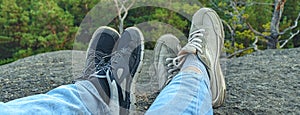 banner with conceptual image of two pairs of legs in sneakers against the background of forest rock. Casual unisex