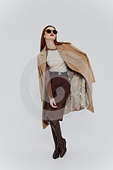 Banner for the design of the showroom clothing brand. Stylish redhead lady in beige coat glasses posing on a white