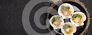 banner with flat lay of baked scallops with caviar and creamy garlic sauce on a black textured background with space for