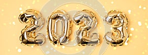 Banner of foil gold air balloons in the form of numbers 2023 on yellow background.