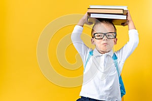 Banner Funny Preschool Child Boy in Glasses with Book on Head and Bag on Yellow Background Copy Space. Happy smiling kid