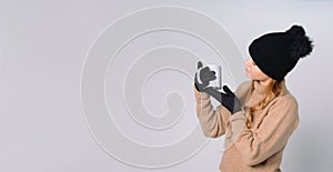 Banner,grey, long format. A girl drinks hot tea and looks at her favorite white cup. Winter clothes, hat and gloves