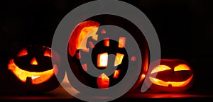 Banner Halloween pumpkin background, three pumpkins with dark black background. Two scary faced pumpkins and house