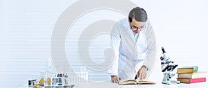 Banner of handsome Asian smart male scientist wearing gown uniform, doing reseach and experiment. There are books, microscope and