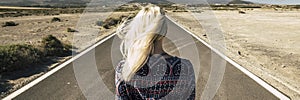 Banner header back view of blonde long hair woman against a long endless asphalt road and desert on both sides. Concept of travel
