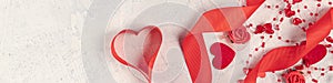 Banner heart from a red ribbon  red hearts  and beads with hearts on a white stone background. Valentine\'s day background.