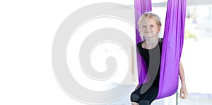 Banner kids Aerial flying yoga exercises. Portrait young smiling girl practice in aero stretching swing in purple