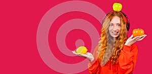 Banner, long format. Happy red-haired girl with hangs listens to music in big headphones and poses with fruits on a red