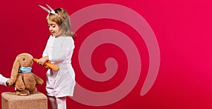 Banner,long format. A little kindergarten girl dressed in a white suit and bunny ears feeds her favorite toy bunny with