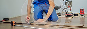 BANNER, LONG FORMAT Man installing new wooden laminate flooring on a warm film floor. Infrared floor heating system