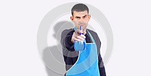 Banner, long format over grey background. Serious male housekeeper wearing blue apron, holding spray bottle towards the