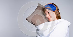 Banner- long format. Young beautiful woman stay wrapped in soft white blanket and pillow in her hands, looking side, isolated