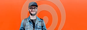 Banner panoramic portrait of smiling hipster guy wearing denim jacket, cap, backpack and glasses isolated on lush lava background.