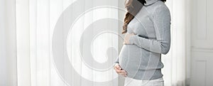 Banner Pregnant Woman turtleneck sweatshirt standing in front of windows and stroking big belly with love at cozy home,Pregnancy