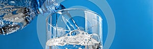 Banner of puring water from plastic bottle into glass on blue background. Stream of clean water flowing in a glass