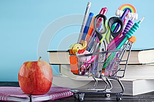 Banner of Shopping cart with school supply on a blue background with a stack of books and an apple with copy space. Back to school