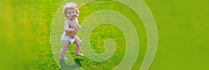 Banner with spring child face. First step. Baby standing barefoot on the green lawn in diaper pants. Kids on green grass