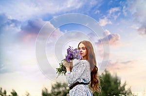 Banner with a stunning young girl looking at the camera, a redhead holding a bouquet of lilac lupins in her hands. Background blue