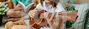 Banner of unrecognizable little girl playing ukulele while boy reading book on handmade shelter tent