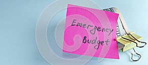 banner with US dollars in paper clip on pastel blue background with note written EMERGENCY FUND : Concept of setting