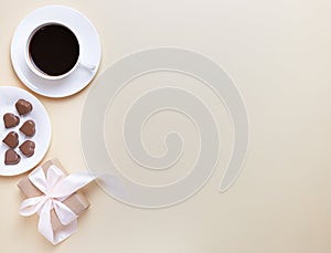 Banner of Valentine`s Day. A Cup of coffee, a gift box and a heart-shaped chocolate on a neutral beige background.