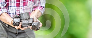 Banner view of coal briquettes in hands of an old man with a green background