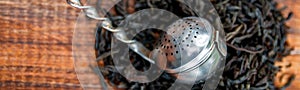 Banner of Vintage strainer with dry leaves of black tea on wooden background