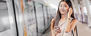 Banner, web page or cover template of Young Asian woman passenger using and listening music via smart mobile phone in subway train