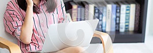 Banner website asian young woman working online laptop with smile and happy sitting on chair at living room, girl using notebook