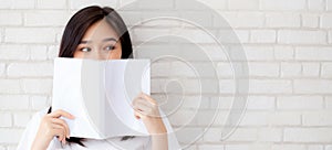 Banner website beautiful portrait asian woman happy hiding behind open the book with cement or concrete background, girl standing