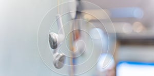 Banner of white earphones hanging off a office partitions. Modern earphones. A modern gadget on a blurred office background