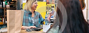 Banner of woman shop assistant registering client data in store terminal to make invoice of purchase