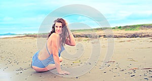 Banner Young brunette girl in striped swimsuit sitting on the beach on the sand Shining bright sun blue sky clouds