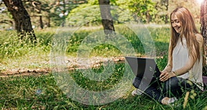 On the banner, a young girl works with a laptop in the fresh air in the park, sitting on the lawn. The concept of remote