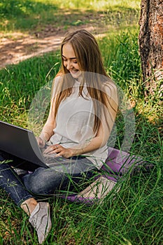 On the banner, a young girl works with a laptop in the fresh air in the park, sitting on the lawn. The concept of remote