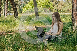 On the banner, a young girl works with a laptop in the fresh air in the park, sitting on the lawn. The concept of remote