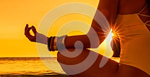 Banner. Young woman practicing yoga on the beach with sunset. Keeps fingers connected, the sun shines through them. The