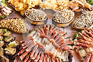 Banquet table with meat products, pistachios, olives, dried fish, chips and other snacks