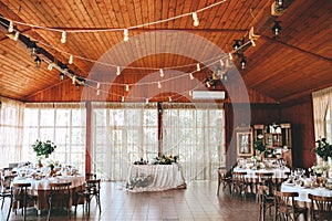 Banquet wooden hall for a rustic wedding with round decorated tables, Viennese chairs with flowered leaves and