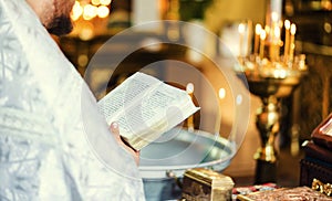 Baptism priest reading from bible during ceremony holding cross.