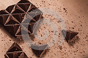 A bar of bitter dark chocolate is broken into pieces lying on the table with cocoa powder