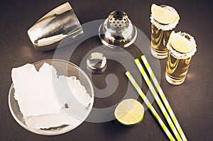 Bar concept: Tequila shots, lime, ice, straws and shaker/Tequila shots, lime, ice, straws and shaker on a dark background. Top
