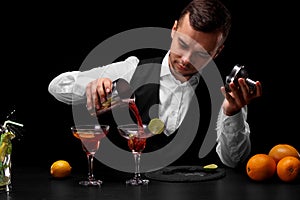 An attractive bartender pours a cocktail in a margarita glass, oranges, lemon, slices of lime on a black background.