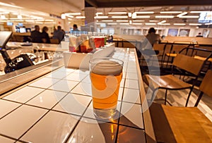 Bar counter with fresh beer in glass at airport lounge area, with some people waiting for the delayed flight