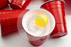 Bar fun, college party and drinking games concept with yellow ping pong ball dropped in red plastic cup while playing beer pong