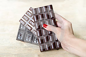 Bar of milk, black and porous chocolate in a woman`s hand like a fan. Warm tone, wooden background